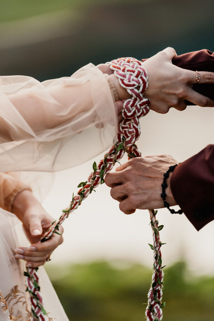 a couple uses a magenta and white gold Celtic hand fasting knot during their elopement ceremony