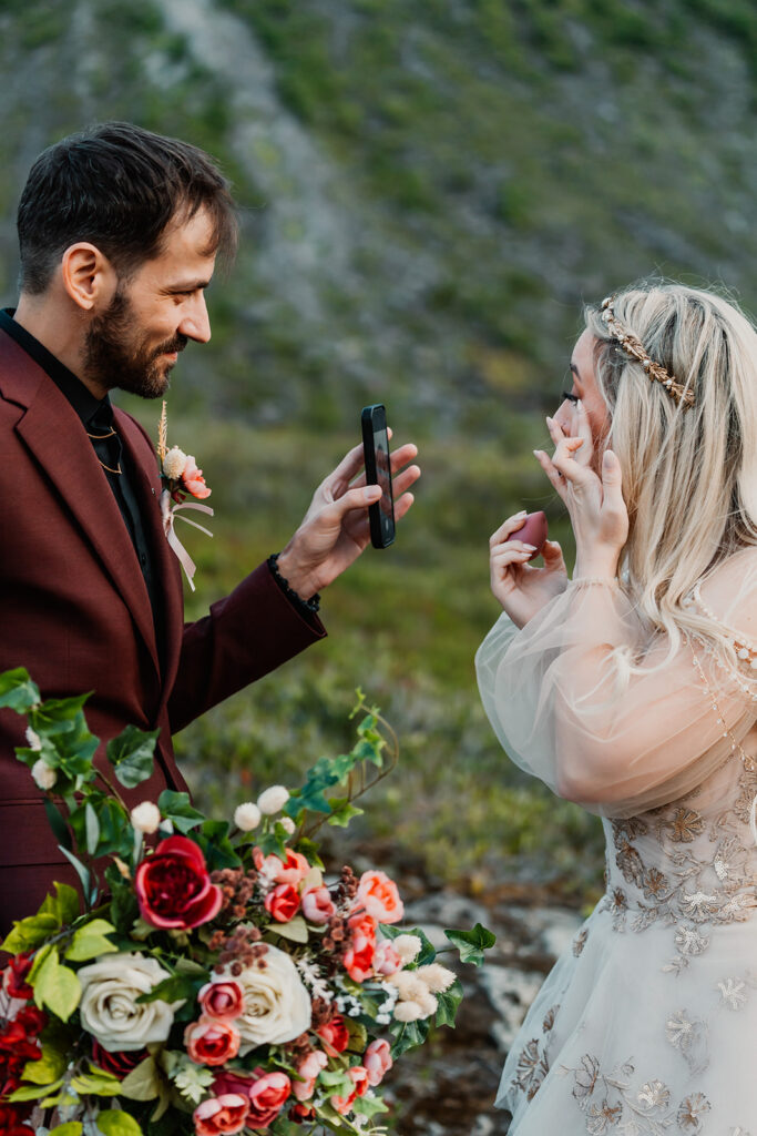 a groom holds up a phone for his bride as she uses it as a mirror to fix her makeup after their ceremony during their mount baker elopement