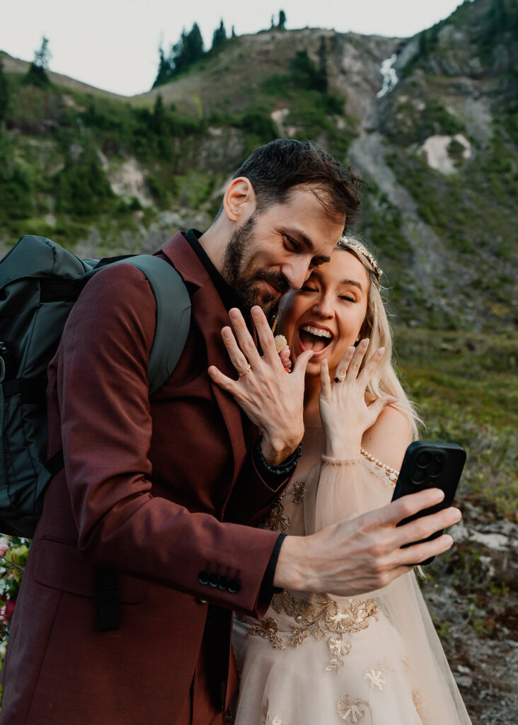 a couple in wedding attire takes a selfie showcasing their freshly placed wedding bands after their mount baker ceremony