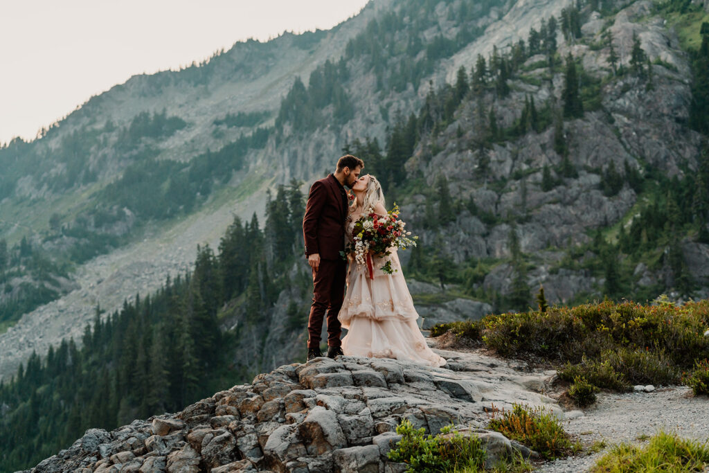 a bride and groom in wedding attire kiss with a stunning mountain backdrop behind them during their mount baker elopement