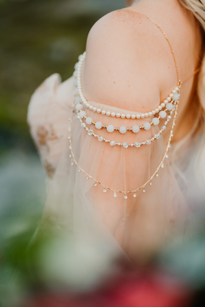 a detail shot of the beading of a brides cape made of carefully strung white and gold beads that hang delicately on her shoulders and upper arms 