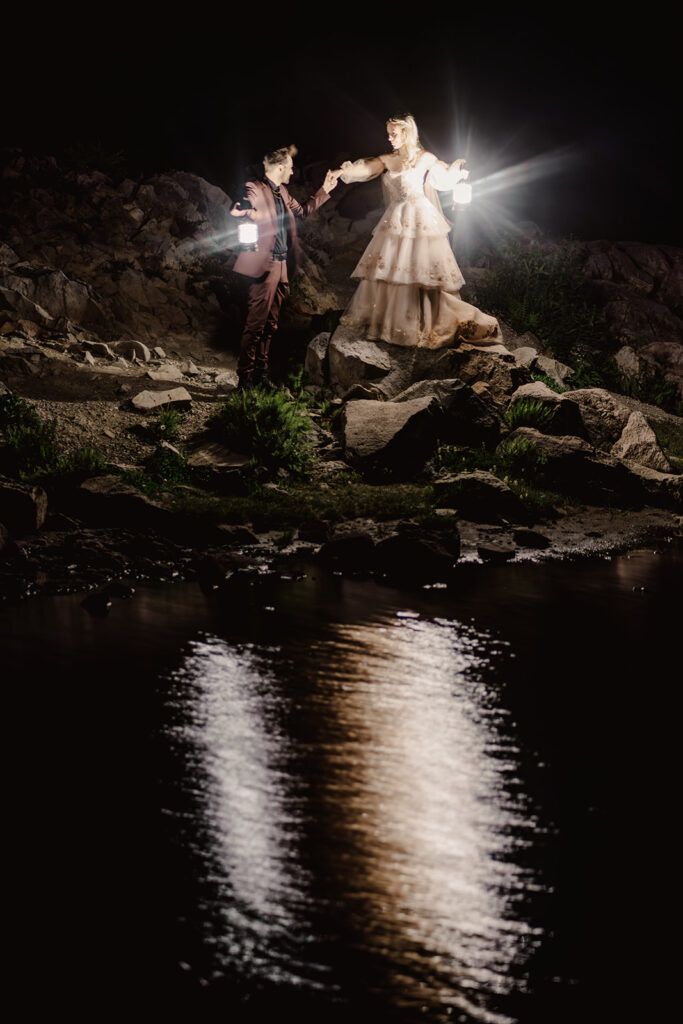 an evening shot of a couple exploring a mountain tarn. They hold lanterns as they explore the landscape during their mount baker elopement