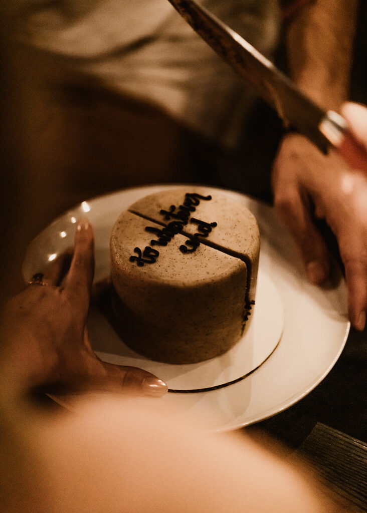 a close up shot of a small wedding cake for this mount baker elopement. we see the hands of the bride and groom around the plate and the script reads "to whatever end"