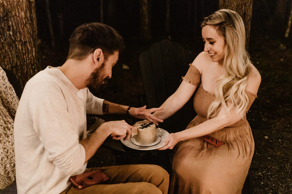 a couple, illuminated by a campfire cut into a small wedding cake to celebrate their mount baker elopement 