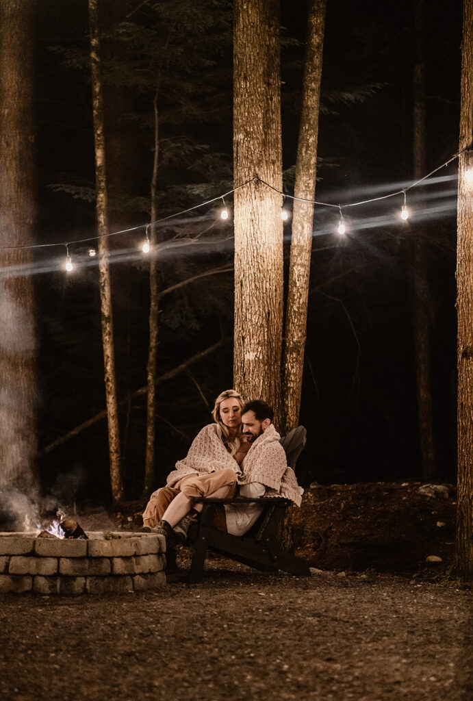 a couple snuggles up by the fire in a knit blanket 