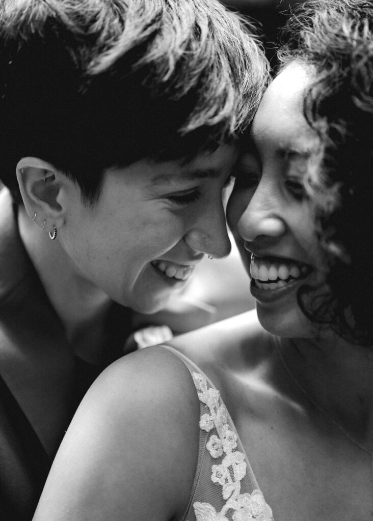 A black and white image of two brides in their wedding attire. The crop is tight on their faces which are snuggled towards each other and radiating joy during their Lake Crescent elopement 