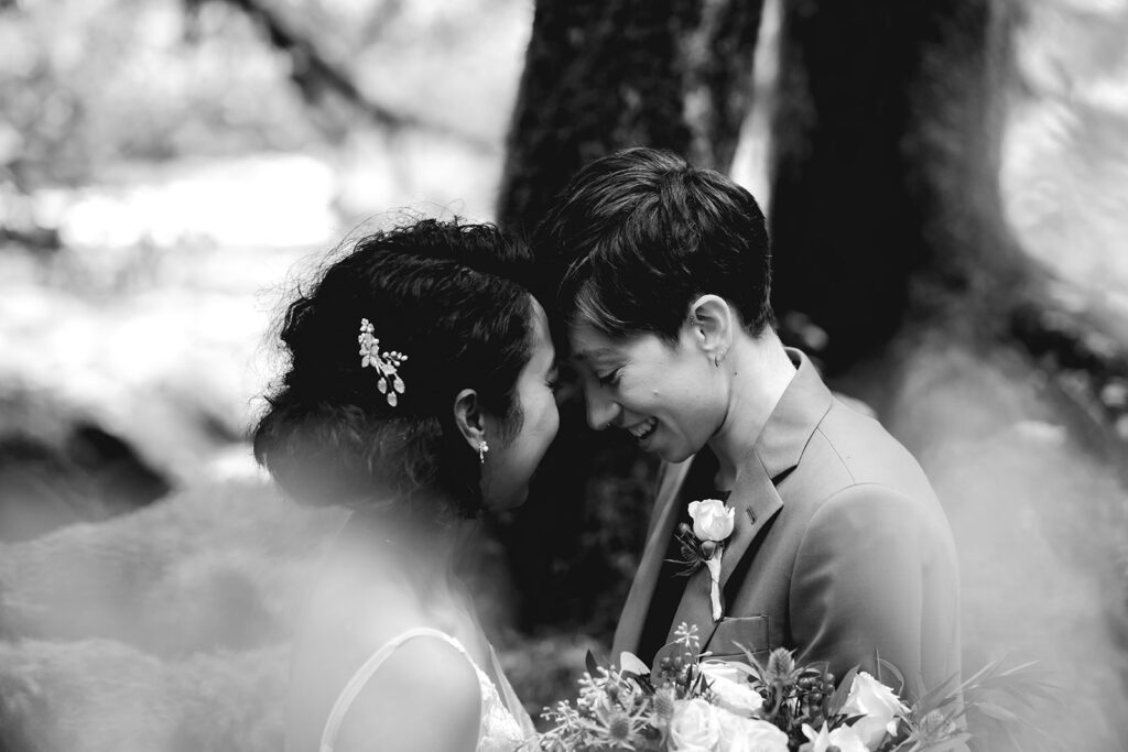 A black and white image of two brides in their wedding attire. The crop is tight on their faces which are towards each other and radiating joy during their Lake Crescent elopement 