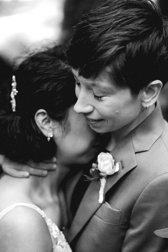 A black and white image of two brides in their wedding attire. The crop is tight on their faces which are snuggled into each other and radiating joy during their Lake Crescent elopement 