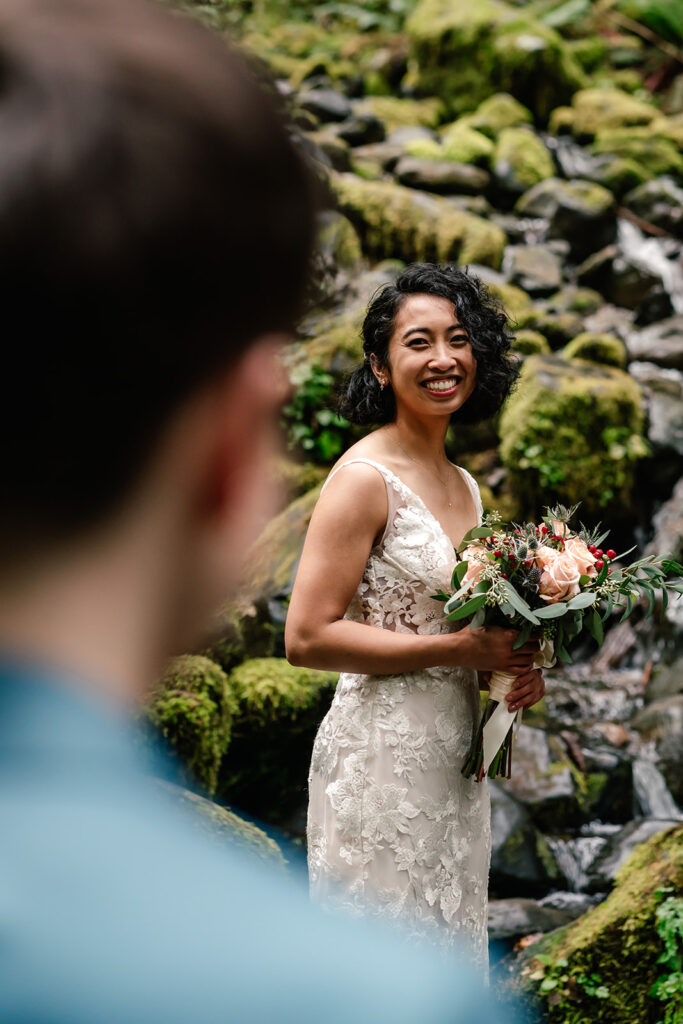 shot over the shoulder, we see a bride smiling at her partner. she is beaming as she gazes at her soon to be bride during their Lake Crescent elopement 