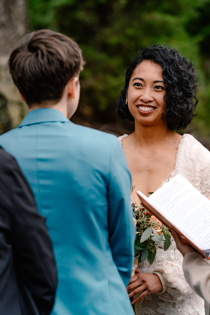 a bride smiles as her partner reads their vows during their lake crescent elopement 