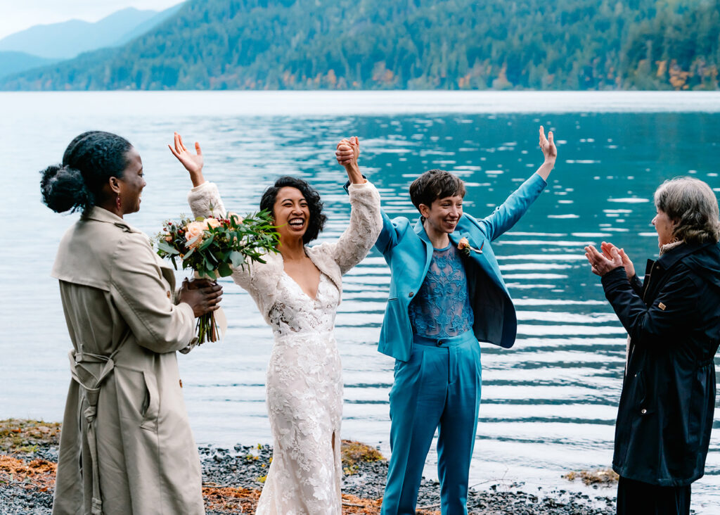 brides and guest celebrate their ceremony with their guests! They throw their hands up with excitement and their guests all clap with joy during this Lake Crescent elopement 