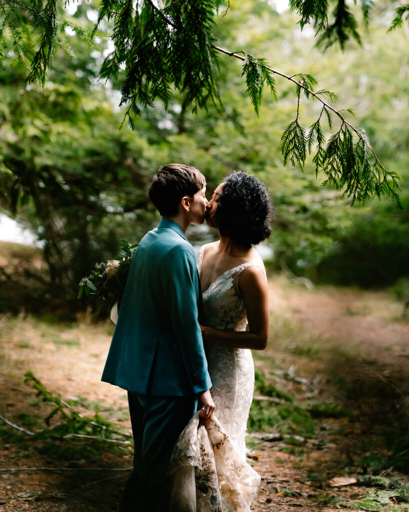 a couple in wedding attire embrace and kiss. they are framed and surrounded by deep greenery and foliage during their lake Crescent elopement