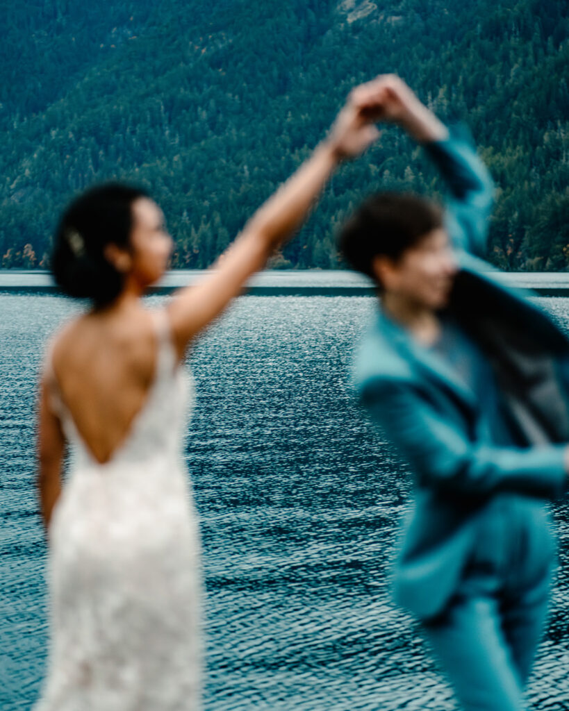 a blurry shot of our brides dancing on the shores of Lake Crescent. The landscape is sharp and our couple is blurry with joyful motion