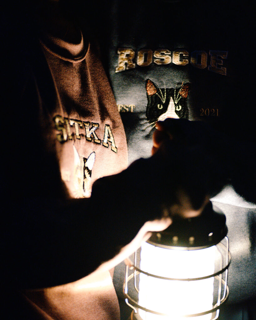 a close up shot of custom sweatshirts with cats embroidered on them illuminated by lantern light 