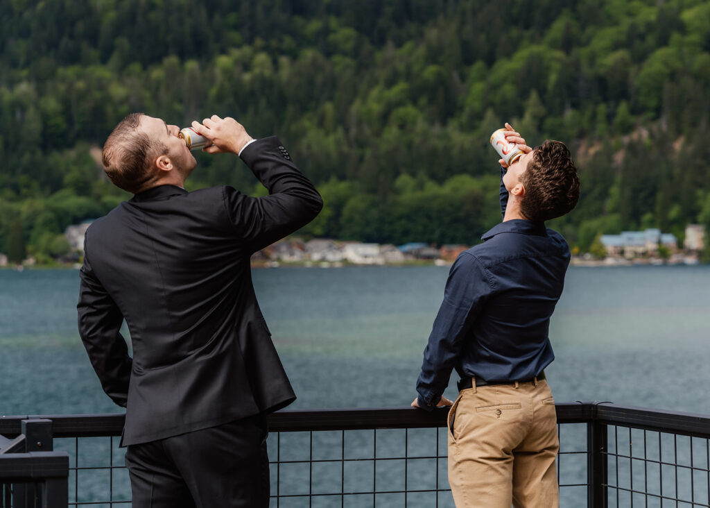 a groom, in his wedding attire, shares a drink with his friend as they finish getting ready for his wedding day