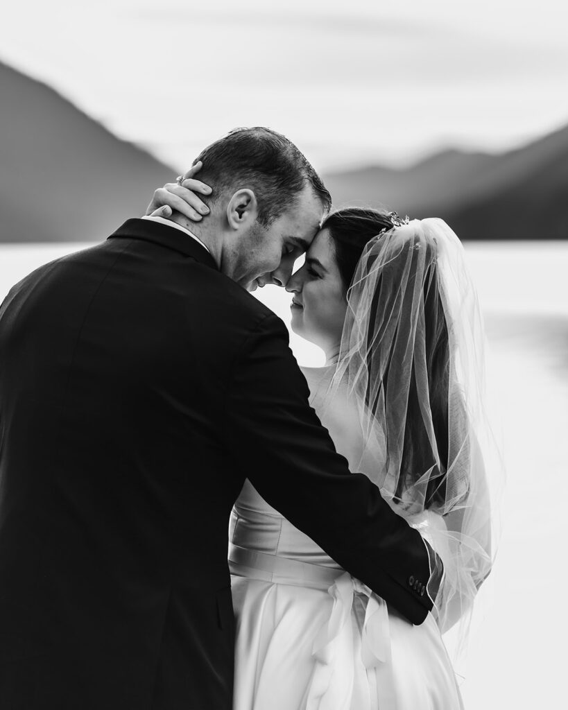 a black and white image of a bride and groom embracing, their faces press against each other as they smile
